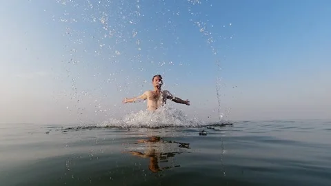 A young man raises splashes of water upward. Water games. Summer and vacati.. Stock Footage 258058254