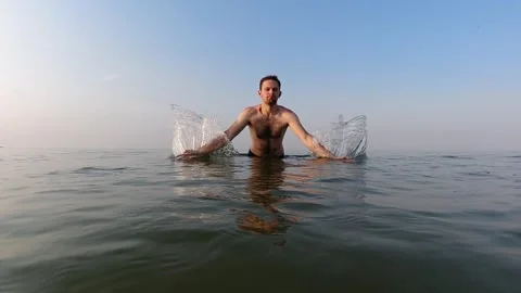 A young man raises splashes of water with both hands. Slow motion. Water ga.. Stock Footage 258586313