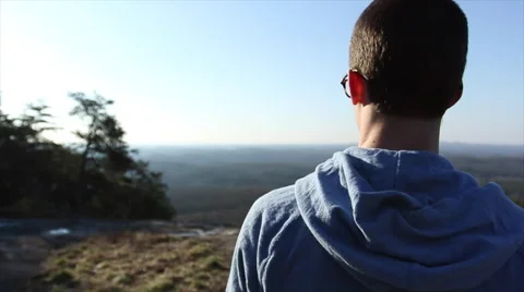 Young man reaching the top and looking out at mountains Stock Footage 63881736