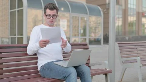 Young Man Reacting to Loss while Reading Documents and Working on Laptop Stock Photos
