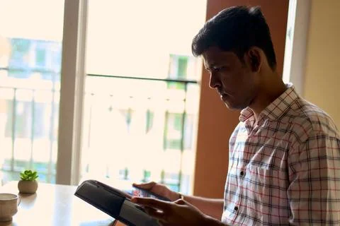 Young man reading attentively while seated indoors near a window with natur.. Stock Photos