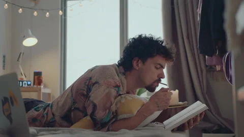 Young Man Reading Book and Smoking a Cigarette on Bed Stock Footage 235656038