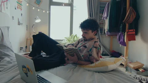 Young Man Reading Book and Resting on Bed Stock Footage 235656336