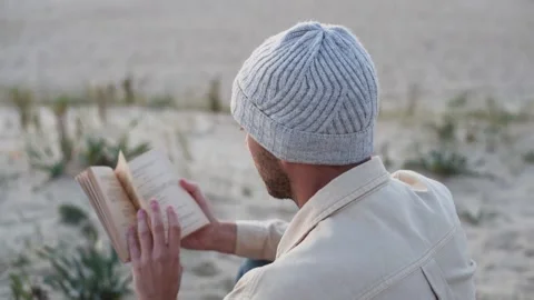 Young Man Reading Book Backward on Beach: Close-Up Shot Stock Footage 263908554