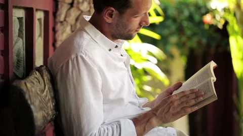 Young man reading book on bench in front of country house HD Vídeo Stock 39974413