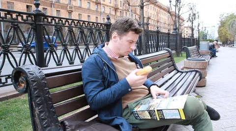Young Man Reading Book On Bench By City Street Stock Footage 55443704