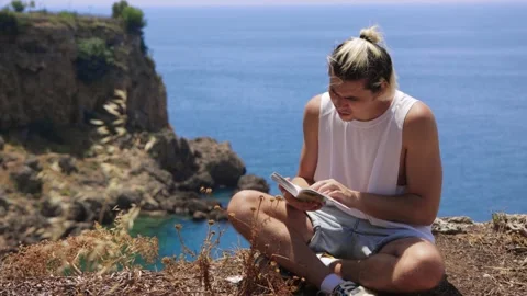 Young man reading book on the cliff edge Stock Footage 205516419
