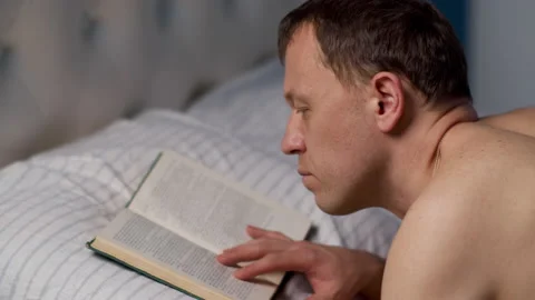 A young man reading a book before going to bed, lying in bed Stock Footage 132501820