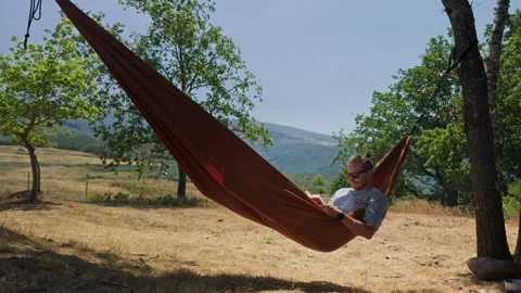Young man reading a book in a hammock in the mountains Vidéo 343656629