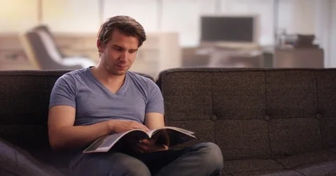 Young man reading a book on his couch Stock Footage 78628148