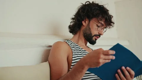 Young Man Reading Book At Home Relaxing On Couch Stock Footage 331408776