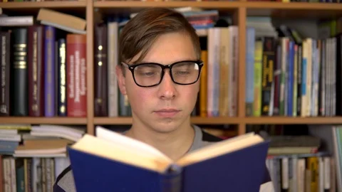 A young man is reading a book in a library. A man with glasses carefully looks Stock Footage 121532367