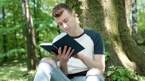 Young man reading book in the park and having painful headache, steadycam shot Stock-Footage 76386894
