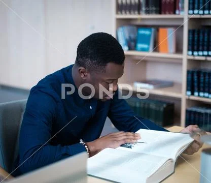 Young Man Reading Book In Public Library