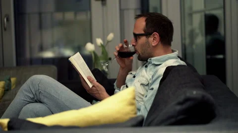 Young man reading book sitting on sofa at home HD Stock Footage 51244318