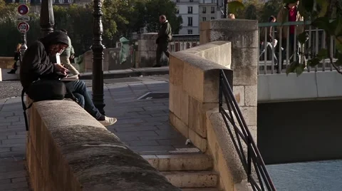 Young man reading book sitting on the wall of a bridge in paris france Stock Footage 65449318
