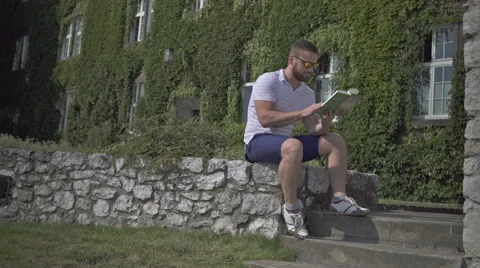 Young man is reading book, sitting on the wall. 動画素材 65524887
