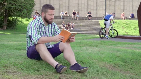 Young man reading book, sitting on grass. Steadicam. 库存影片 67237514