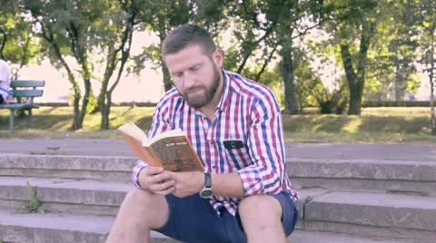Young man reading book, sitting on stairs. Slider and pan shot. Vídeo Stock 67245243