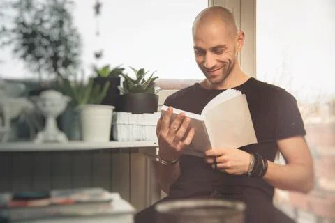 Young man reading a book, sitting on a chair in his living room Stock Photos