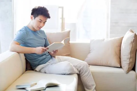 Young man reading a book on the sofa Stock Photos