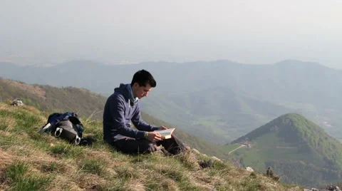 Young man reading a book in solitude in the mountains Stock Footage 49590365
