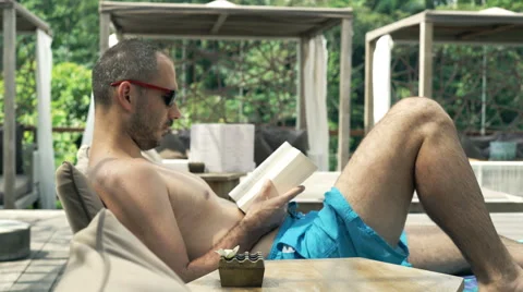 Young man reading book on sunbed, 4K Stock Footage