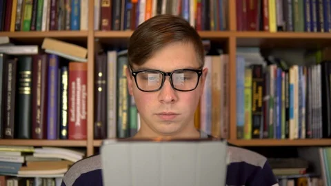 A young man is reading a book in a tablet. A man with glasses carefully looks at Stock Footage 121533021