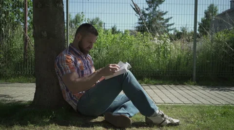 Young man reading book under tree. Vidéo 52689182