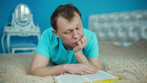 Young man reading book while lying on bed, relaxation concept Stock Footage 145911781