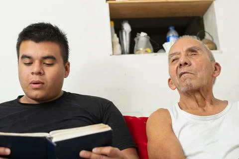 Young man reading book while elderly father listens attentively beside him .. 写真素材