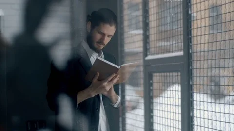 Young man reading book by window at home Stockbeeldmateriaal 71407340