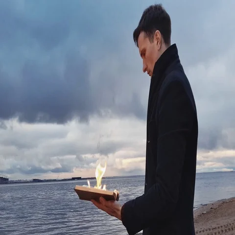 Young man reading burning book standing on coast storm clouds on background Stock Footage 69121705
