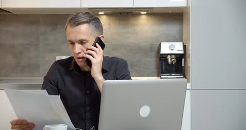 Young man reading a contract or report and talking on the phone at home Stock Footage 126725634
