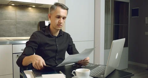Young man reading a contract or report and talking on the phone from home office Stock Footage 128100593