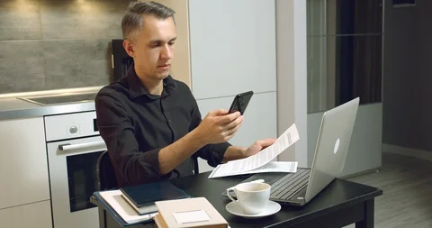 Young man reading a contract or report and talking on the phone from home office Stock Footage 128107945