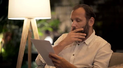 Young man reading documents, bills sitting on sofa at night at home Vídeo Stock 67576386