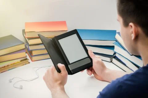 A young man is reading an e-book on the background of old paper books. Stock Photos