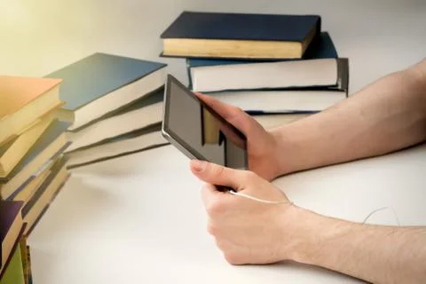 A young man is reading an e-book on the background of old paper books. Stock Photos
