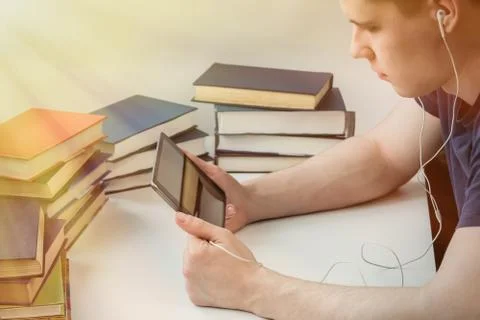 A young man is reading an e-book on the background of old paper books. Stock Photos