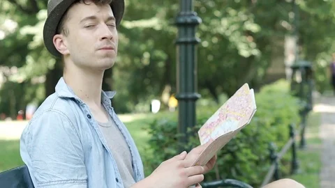 Young man reading map in the park and looks lost, steadycam shot Video stock 79415569