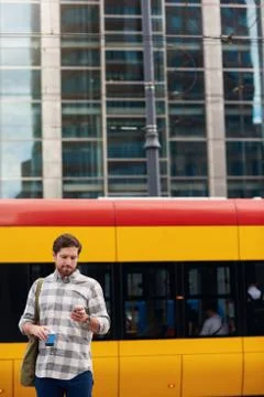 Young man reading messages while standing at a bus stop Foto stock