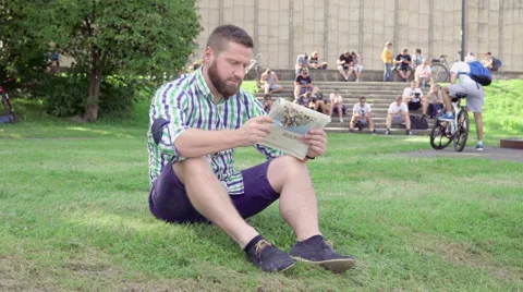 Young man reading newspaper, sitting on grass. Steadicam. 库存影片 67237027