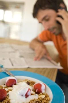 Young man reading newspaper, using mobile phone, strawberries and cereals in Stock Photos