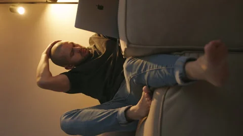 Young man reading the screen of a laptop computer while relaxing on a Stock Footage 256966247