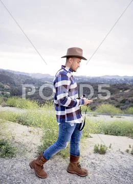 Young Man Reading Smartphone Text On Rural Hill
