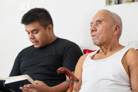 Young man reading while elderly father sits beside him sharing quiet suppor.. Stockfoto's