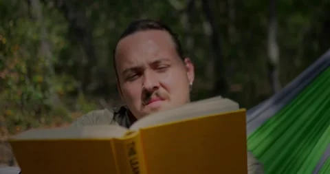 Young Man Reading Yellow Book In Green Hammock... Stock Footage 331820761