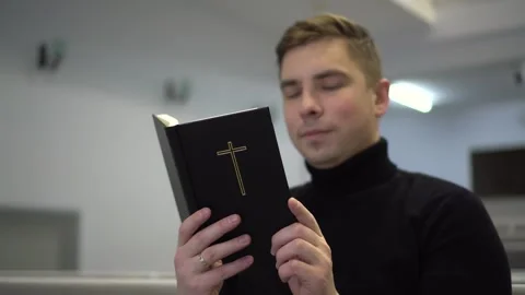 A young man reads the Bible while sitting on a church bench. A Protestant man Stock Footage 255163012