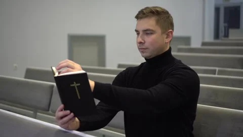 A young man reads the Bible while sitting on a church bench. A Protestant man Vídeos de archivo 256526461